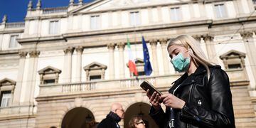 A woman wearing a face mask checks her phone outside the Teatro alla Scala in Milan