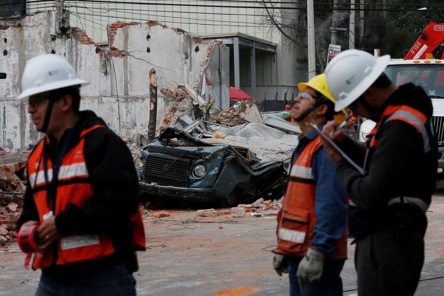 Men work near a damaged wall and a  vehicle after an earthquake in Mexico City