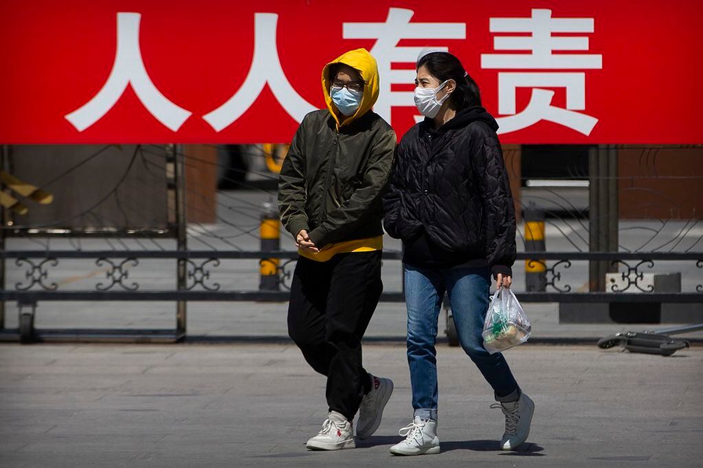 People wearing face masks to protect against the spread of the new coronavirus walk in front of a propaganda billboard reading "it is everyone's responsibility to control the spread of disease" at a public park in Beijing, Tuesday, April 21, 2020. China reported about a dozen coronavirus cases Tuesday, about half of them in the province of Heilongjiang that borders Russia. (AP Photo/Mark Schiefelbein)