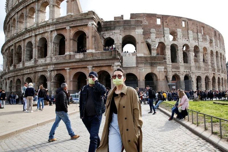 La imagen muestra a una turista frente al Coliseo Romano, usando una mascarilla para evitar la infección