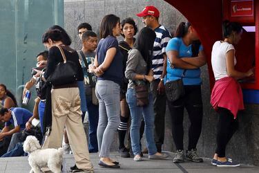 People line up to withdraw cash from an automated teller machine (ATM) outside a Banco de Venezuela branch in Caracas