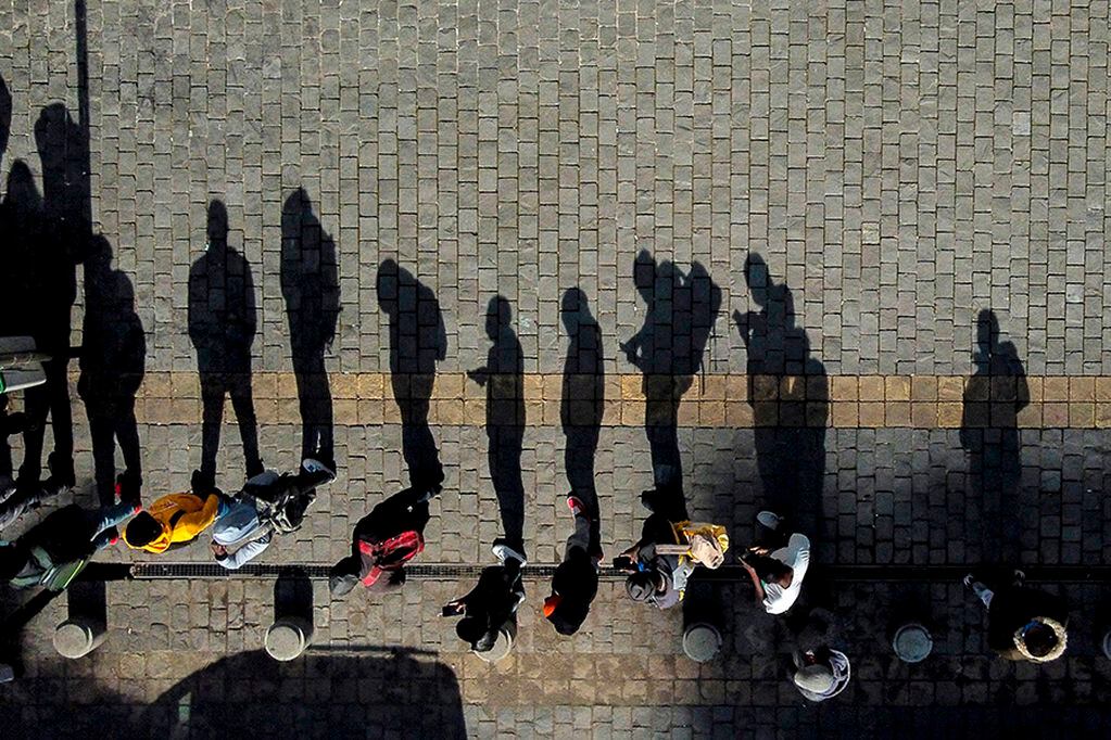 Aerial view of the shadows of people queueing to enter a branch of the pension funds office to request information about the withdrawal of ten percent of their deposits, being cast on the pavement, in Santiago, on July 24, 2020. - Chile's Congress on Thursday approved a law allowing citizens to withdraw up to ten percent of their pension funds to help mitigate the effects of the coronavirus, delivering a political blow to President Sebastian Pinera, who opposed the measure. (Photo by MARTIN BERNETTI / AFP)