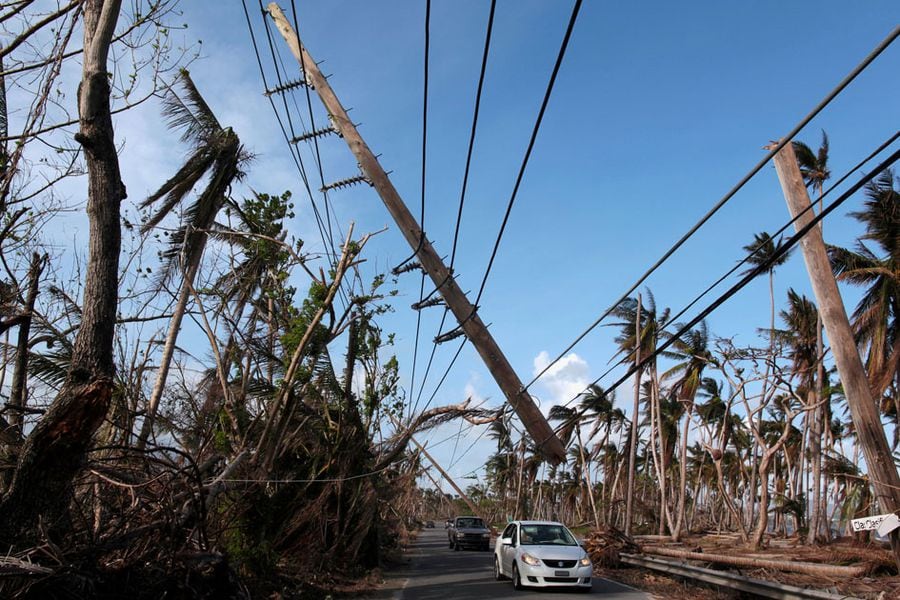 FILE PHOTO: Cars drive under a partially collapsed utility pole, after the island was hit by Hurricane Maria in September, in Naguabo