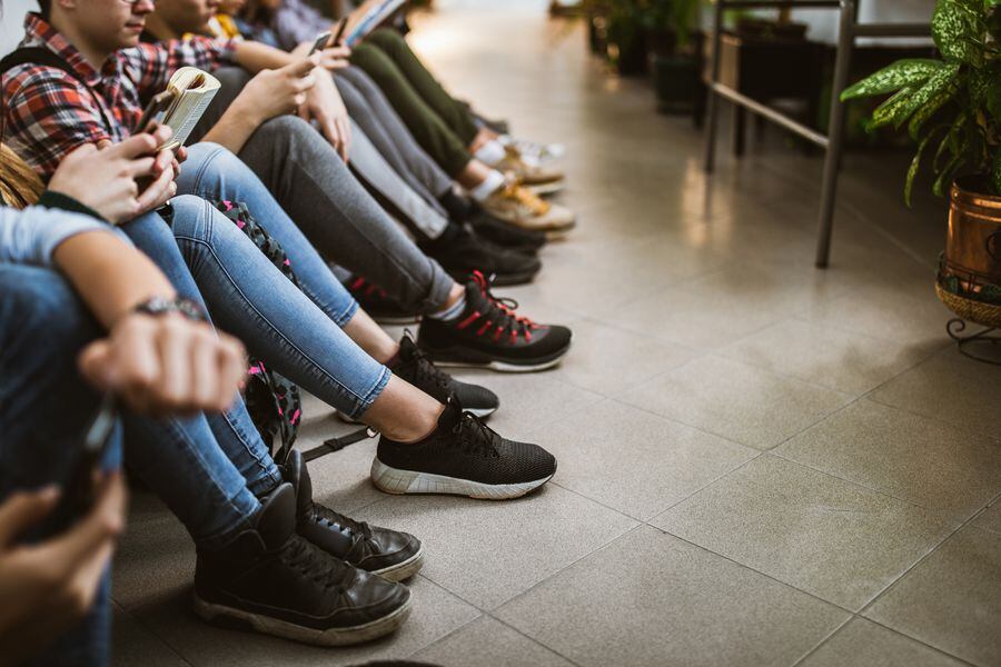 Large group of unrecognizable students relaxing on the floor in a hallway.