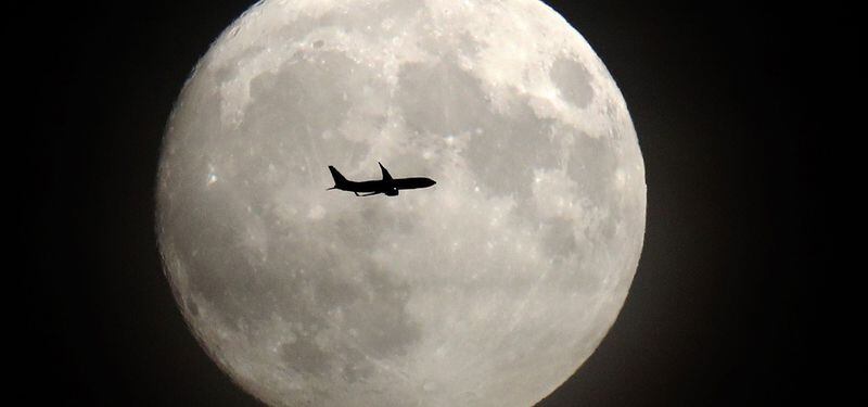 A commerical jet flies in front of the moon on its approach to Heathr