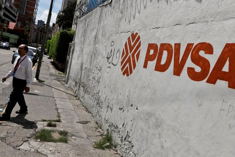 A man walks past a mural with the corporate logo of the state oil company PDVSA in Caracas