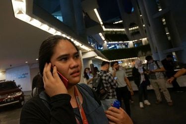 A woman  uses a phone as she leaves an office building, following an earthquake hit in Jakarta