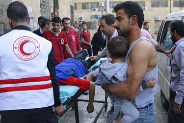 A Syrian man carries a child as they await treatment at a hospital in