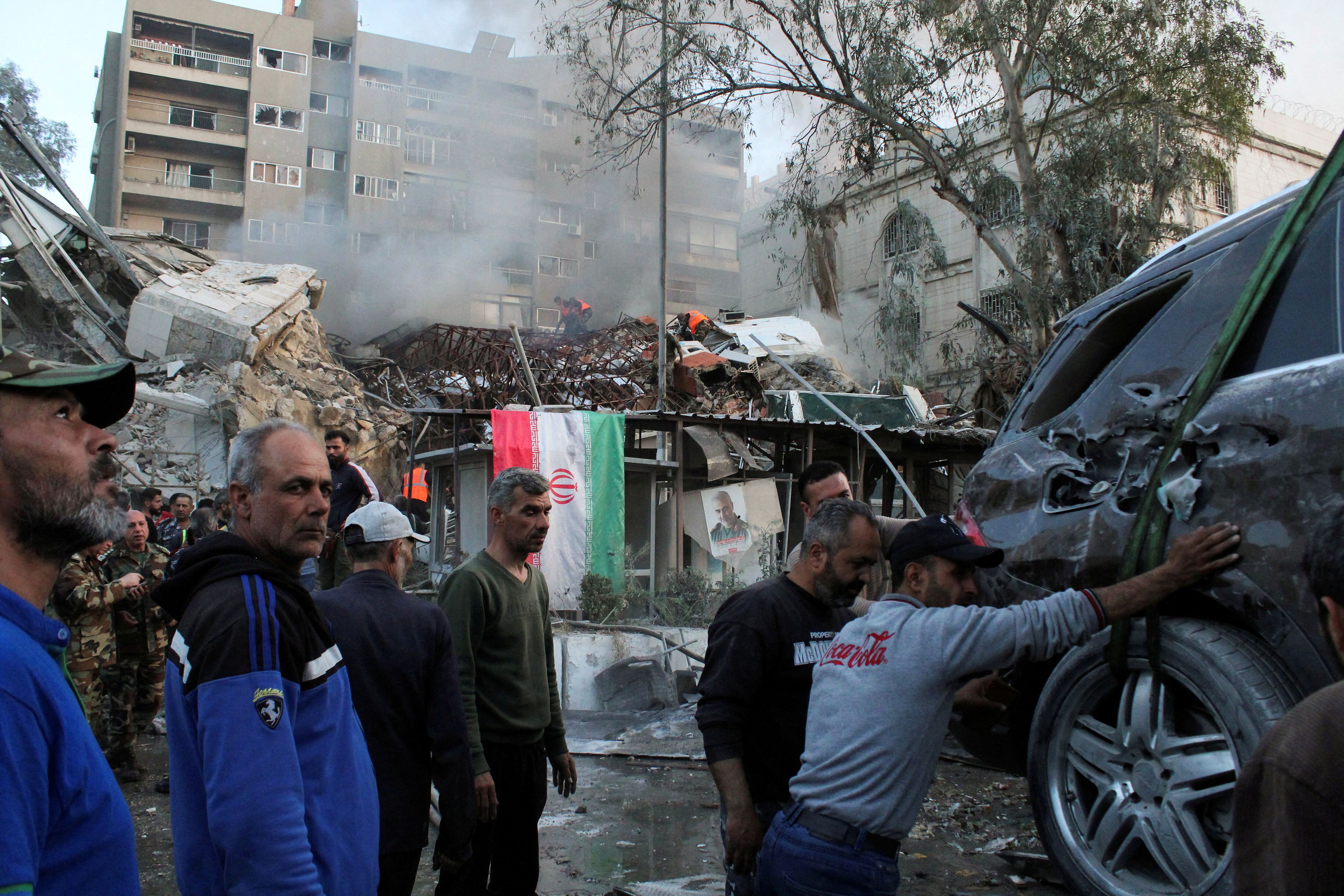 Gente se reúne cerca de un sitio dañado, transportando un vehículo destruido, después de un ataque contra el consulado de Irán en la capital siria, Damasco, el 1 de abril de 2024. REUTERS