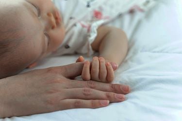 The newborn baby sleeps and grabs the mother's finger