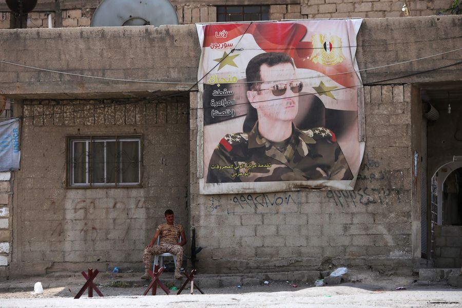 A Syrian soldiers sits next to poster of the Syrian president at the
