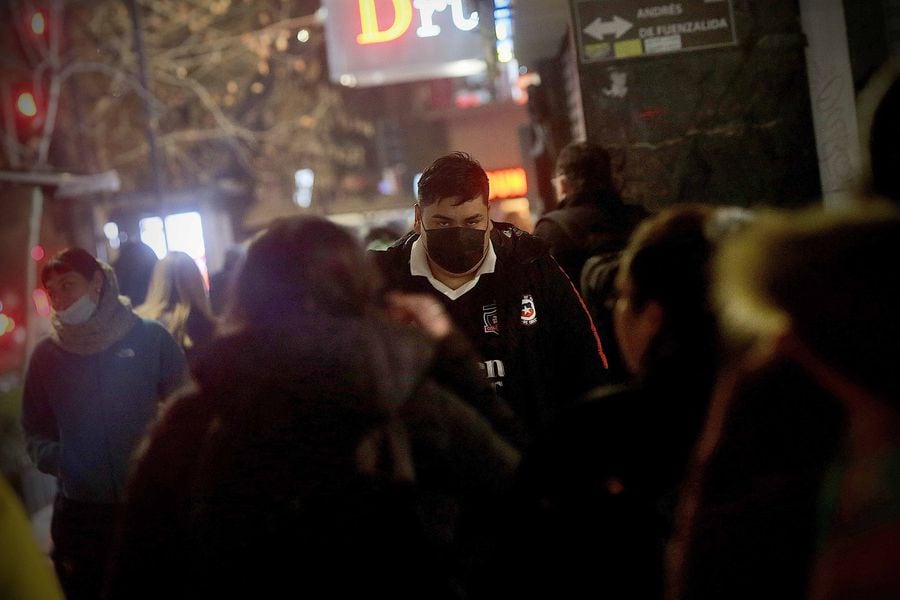 Foto del joven entre la multitud de noche, con mascarilla por motivo de la pandemia por covid-19.