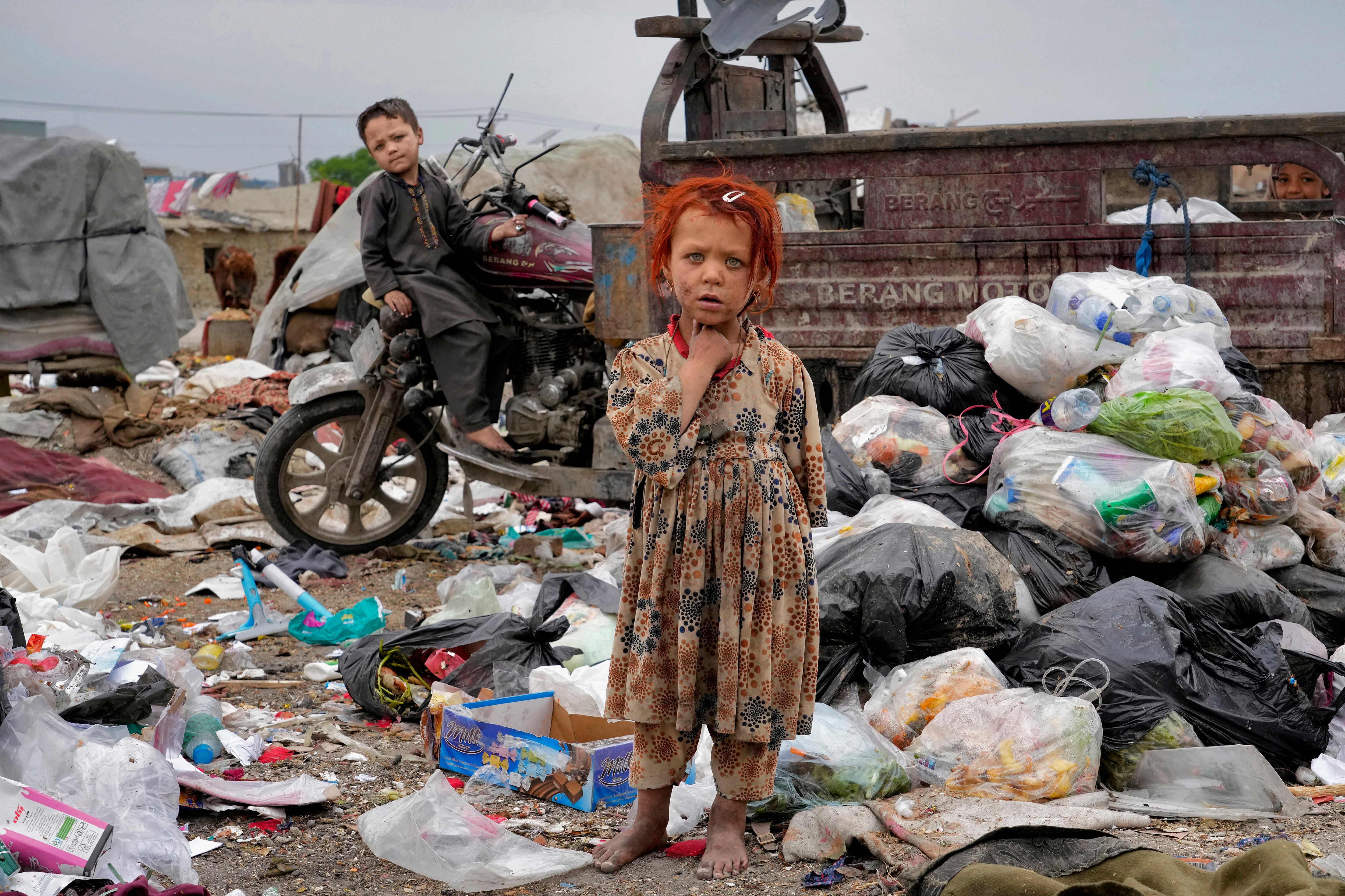 Dos niños afganos permanecen de pie entre montones de basura junto a su vivienda en Kabul, Afganistán, el lunes 18 de abril de 2022.