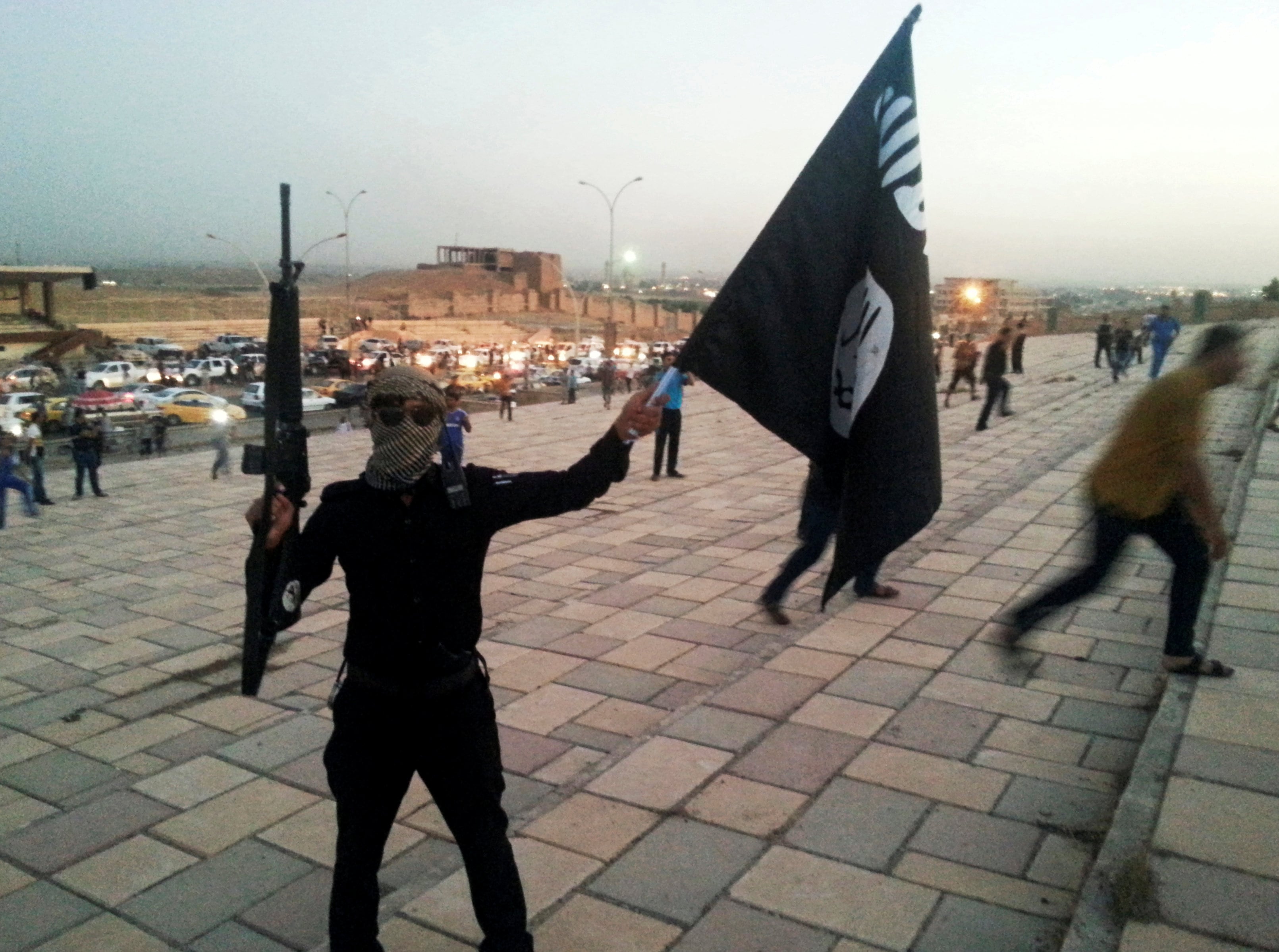 Un combatiente del Estado Islámico de Irak y el Levante sostiene una bandera del grupo y un arma en una calle de la ciudad de Mosul, Irak, el 23 de junio de 2014. Foto: Archivo