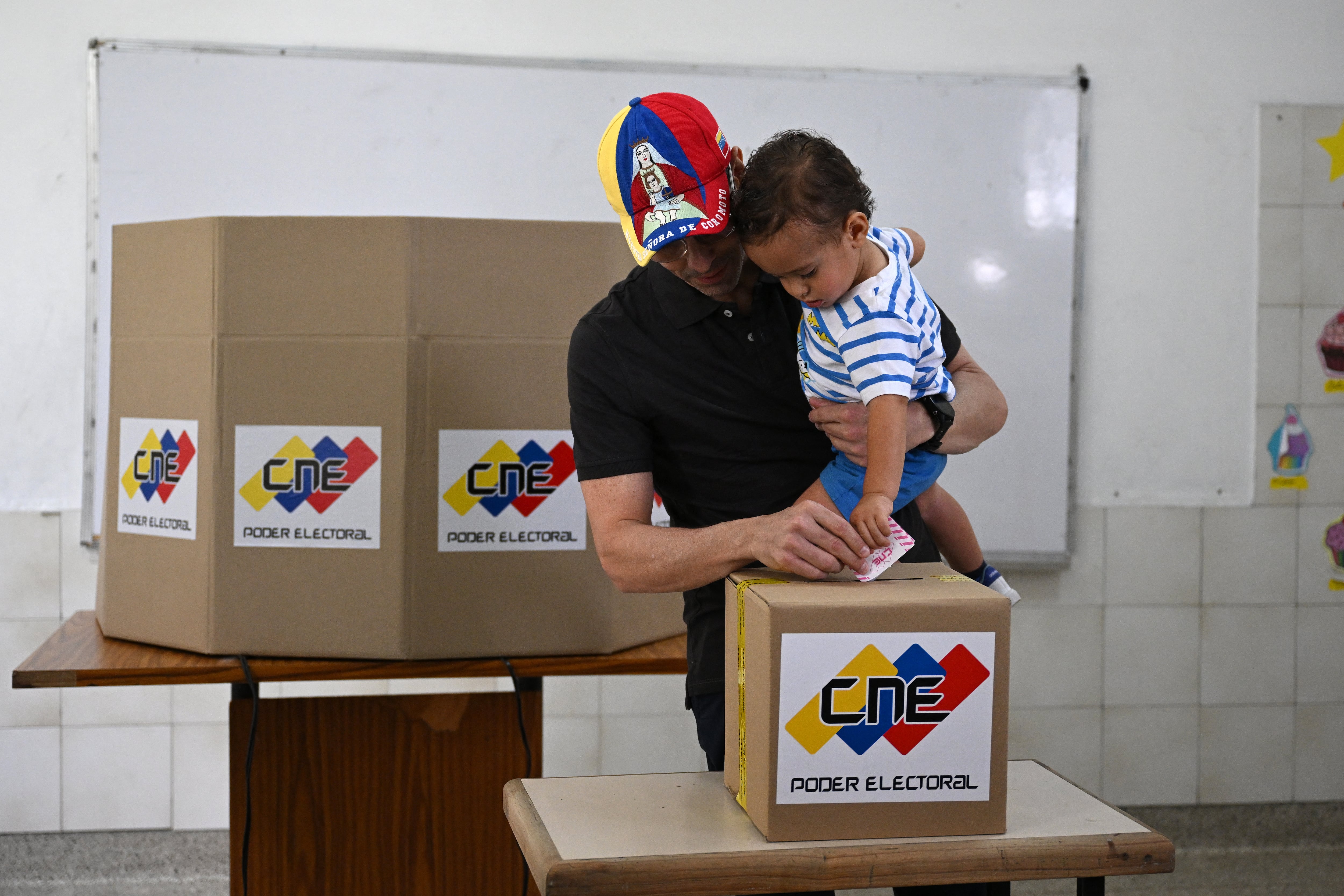El líder opositor y candidato a diputado venezolano, Henrique Capriles Radonski, emite su voto mientras sostiene a su hijo en un colegio electoral de Caracas. Foto: AFP