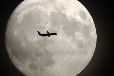 A commerical jet flies in front of the moon on its approach to Heathr