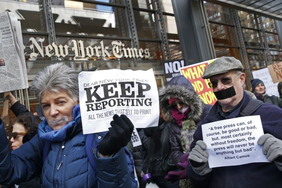 People with taped mouths hold signs and a copy of the New York Times